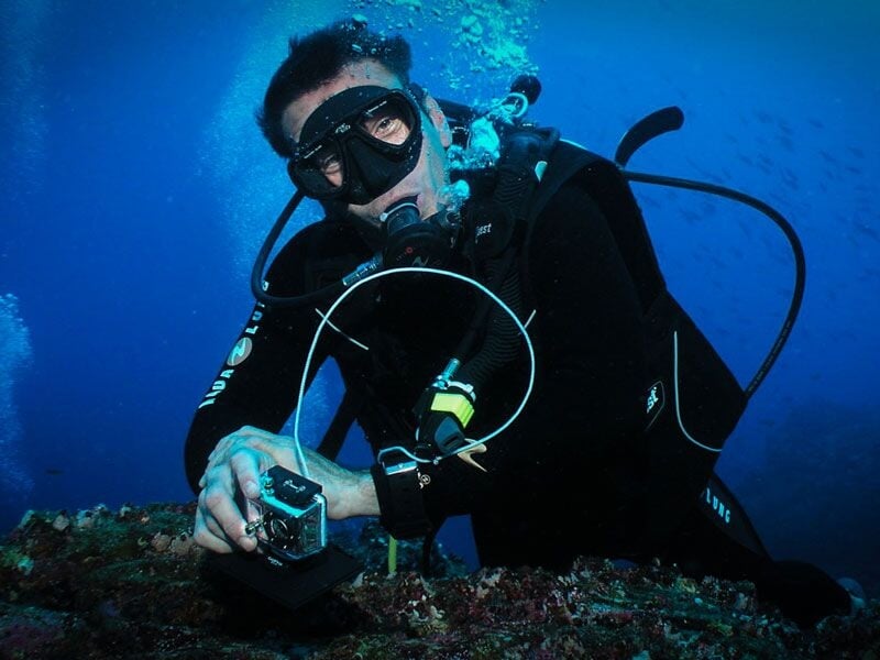 Plongeur équipé d'un masque et d'un tuba sous l'eau, tenant une caméra pour filmer la vie marine.