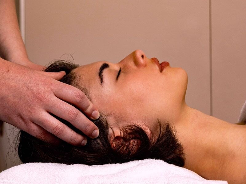 Personne allongée recevant un massage relaxant de la tête dans un spa calme et apaisant.
