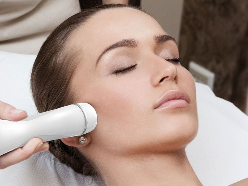 Femme recevant un soin du visage avec un appareil moderne dans un institut de beauté.