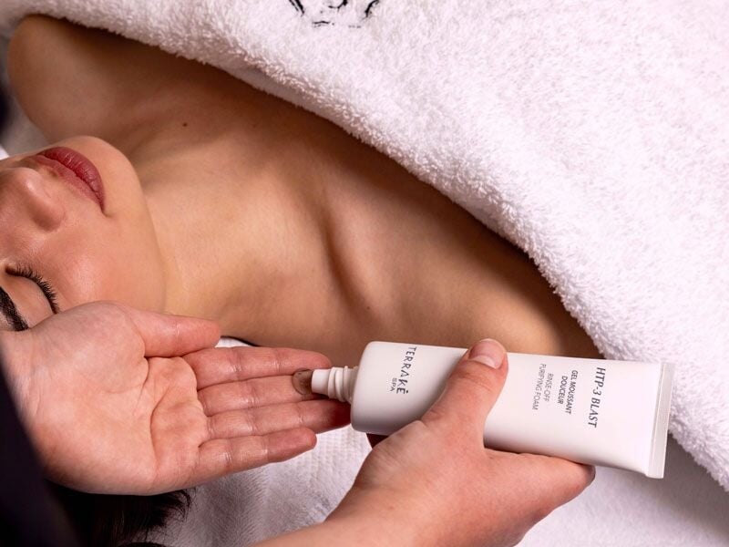 Application d'une crème hydratante sur la main d'une personne allongée sous une serviette.