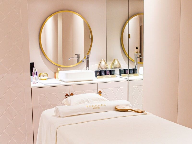 Salle de soin lumineuse avec table de massage, miroir rond et décoration épurée.