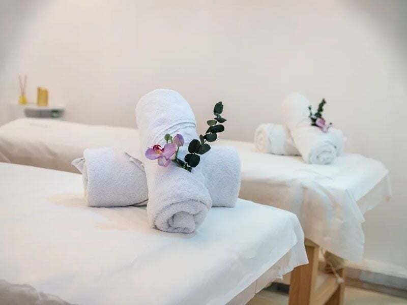 Serviettes blanches roulées décorées avec une orchidée et une branche verte sur une table de massage.