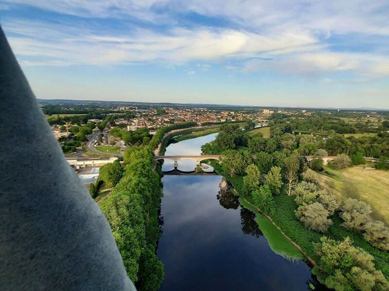 Vue aérienne d'une rivière sinueuse traversant une ville et des espaces verts sous un ciel partiellement nuageux.