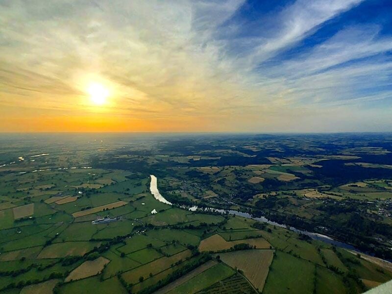 Paysage rural vu d'en haut avec un soleil couchant, une rivière et des champs verts à perte de vue.