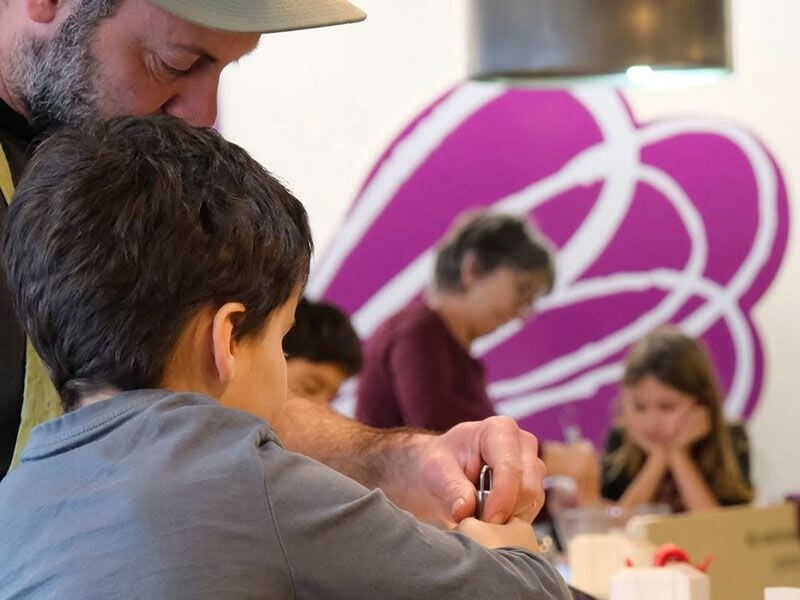 Un adulte montre à un enfant comment utiliser un ustensile de cuisine dans un atelier convivial et coloré.