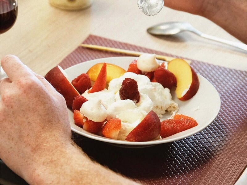 Une assiette de fruits frais avec des fraises, des pêches et une crème blanche servie sur une table.