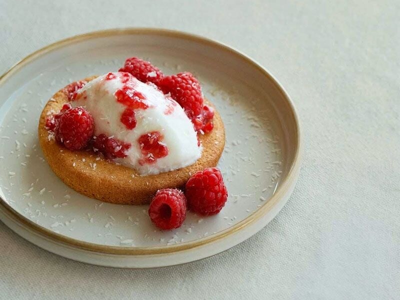 Un dessert composé d'un biscuit rond garni de crème et de framboises fraîches sur une assiette.