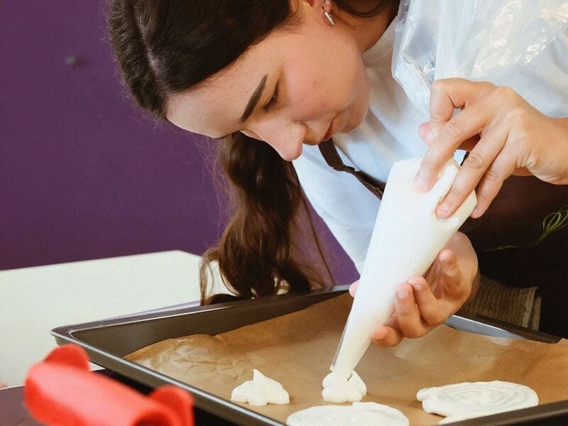 Une jeune femme décore une plaque de cuisson avec une poche à douille remplie de crème.