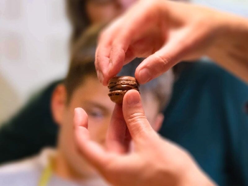 Une personne tient délicatement un macaron au chocolat devant un groupe attentif.