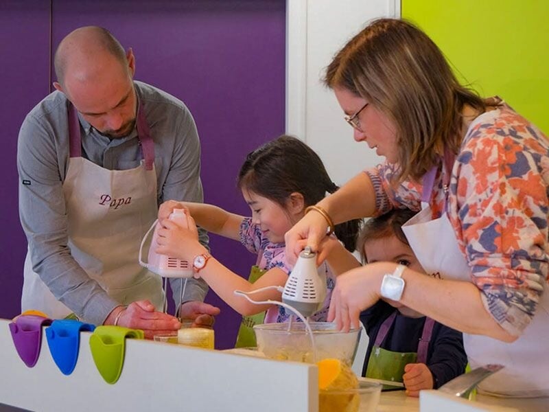 Une famille avec enfants utilise des mixeurs électriques pour préparer une recette en cuisine.