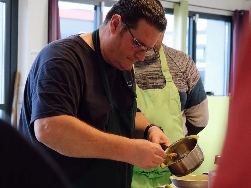 Un homme concentré verse un ingrédient dans une casserole lors d'un cours de pâtisserie.