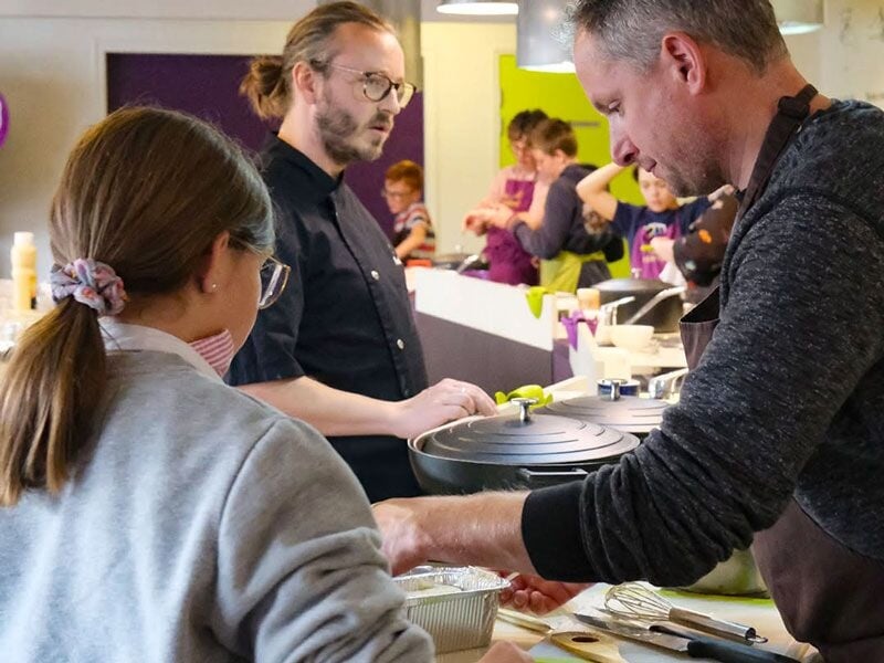 Un chef explique une technique culinaire à un groupe de participants dans un atelier.