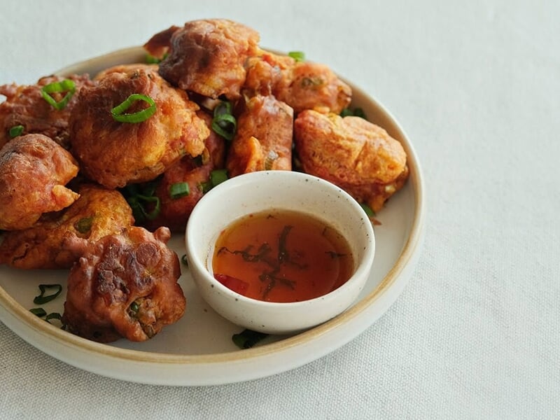 Assiette de beignets dorés accompagnés d'une sauce dans un petit bol, présentée sur une table claire.