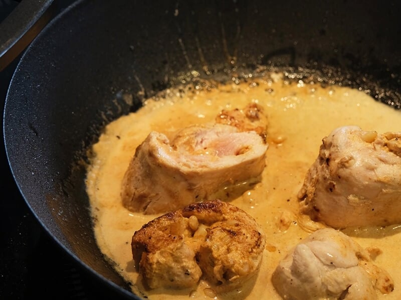 Des morceaux de viande cuisent dans une poêle avec une sauce crémeuse, en train de mijoter doucement.