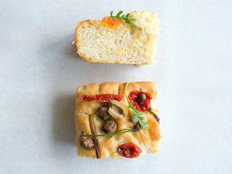 Deux morceaux de focaccia garnis de légumes et herbes, présentés sur une surface claire et épurée.