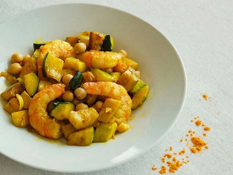 Un plat coloré de crevettes, pois chiches et légumes sautés, joliment présenté dans une assiette blanche.