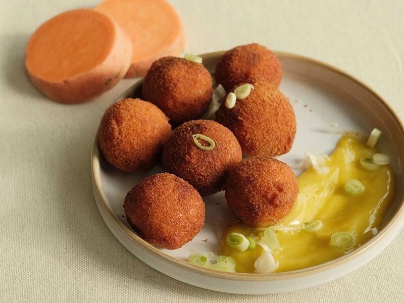 Des croquettes dorées servies avec une sauce jaune, disposées sur une assiette claire avec des rondelles de légumes.