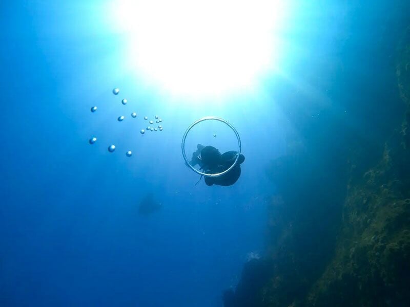 Plongeur sous-marin entouré de bulles, vu de dessous avec le soleil brillant à la surface de l'eau.