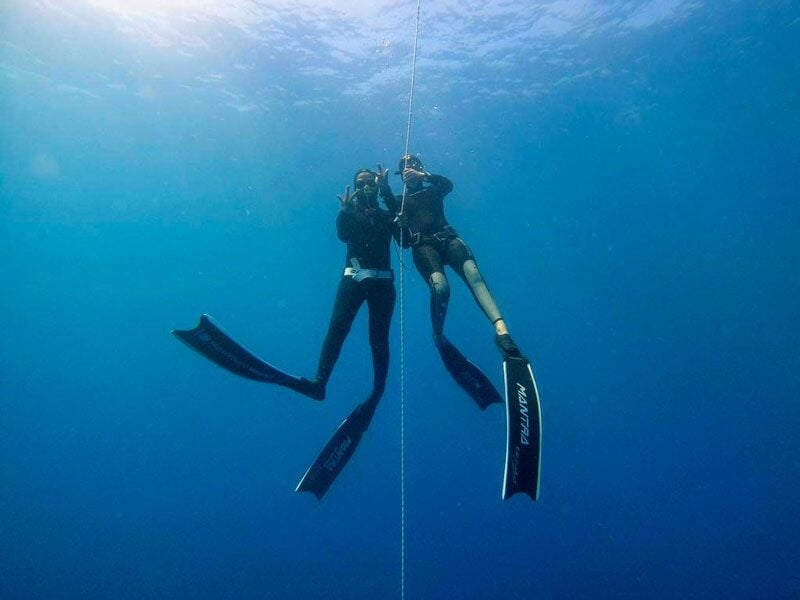 Deux plongeurs en combinaison noire descendent le long d'une corde dans une eau bleue profonde.