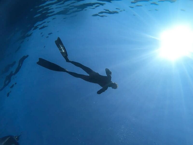 Plongeur solitaire nageant sous l'eau avec le soleil brillant à la surface dans une mer bleue profonde.