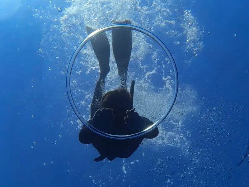 Plongeur sous-marin vu de dessous, entouré de bulles, avec un cercle transparent devant lui.