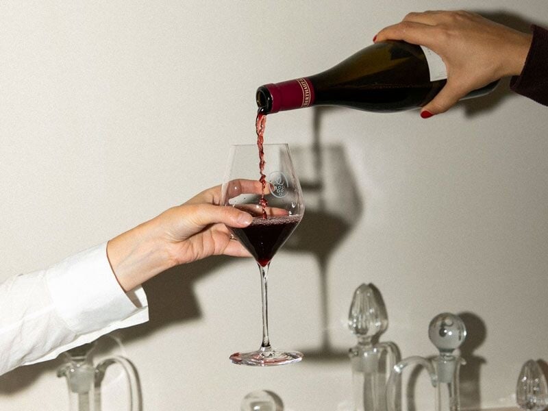 Vin rouge versé dans un verre tenu par une main, prêt pour une dégustation conviviale et raffinée.