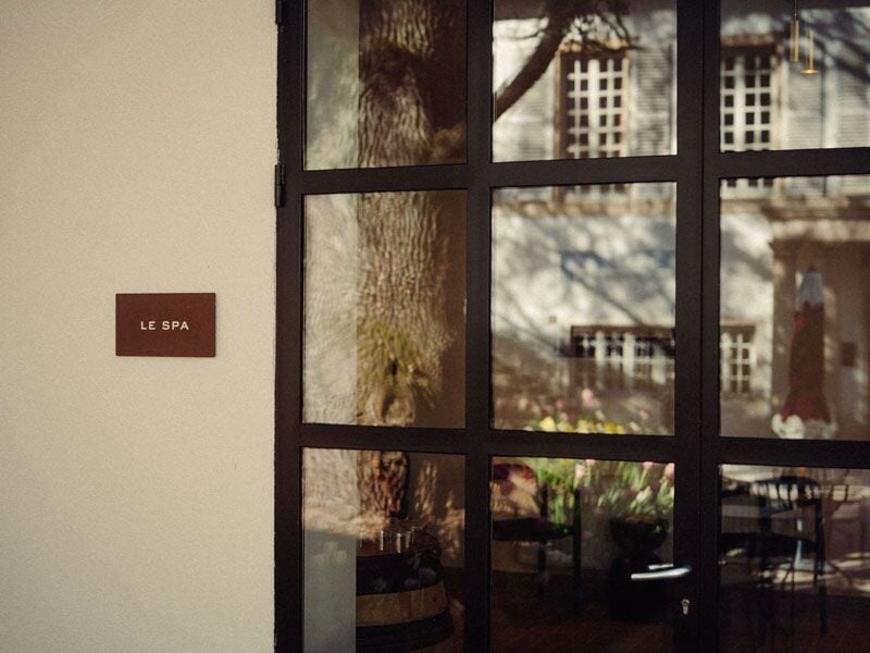 Entrée du spa avec une porte vitrée reflétant un arbre et un bâtiment en arrière-plan