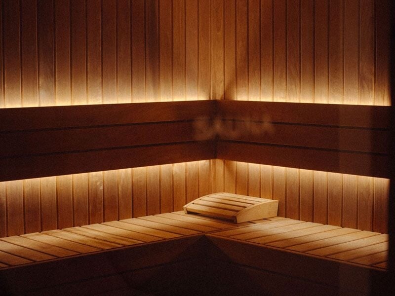 Intérieur d'un sauna en bois avec un coussin posé sur un banc d'angle éclairé par une lumière douce