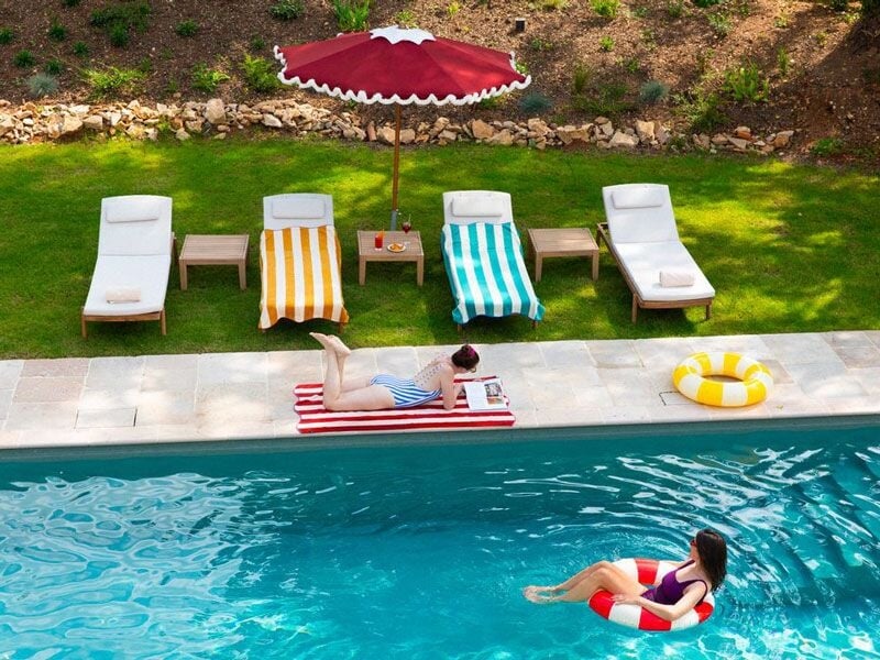 Piscine extérieure avec des transats colorés et une personne allongée lisant au bord de l'eau