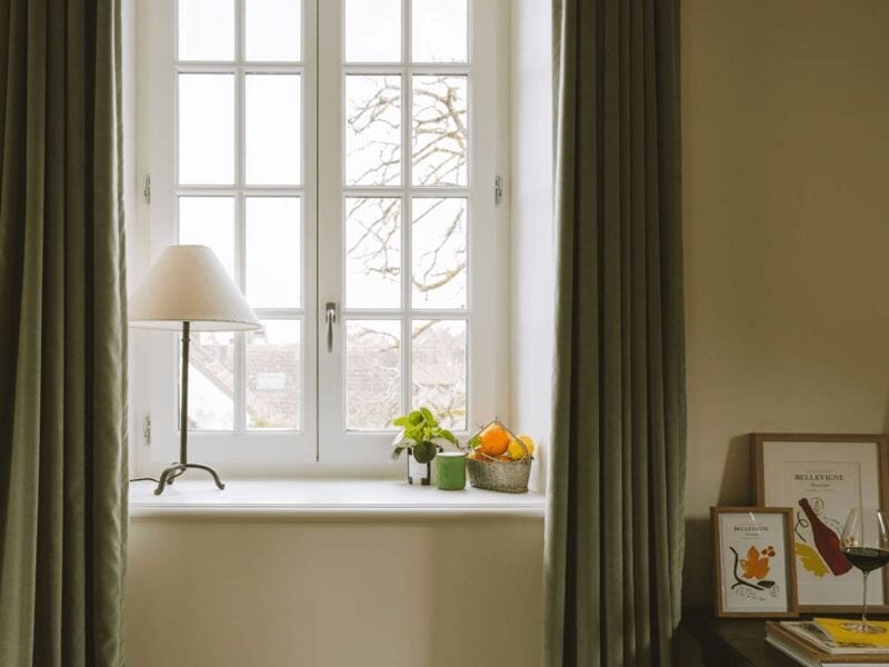 Fenêtre blanche avec rideaux verts, plantes et corbeille de fruits sur le rebord, décor minimaliste
