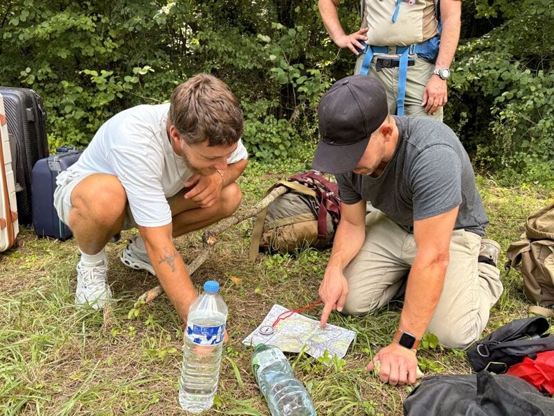 Deux hommes en plein air étudiant une carte pour s'orienter, entourés de sacs et bouteilles d'eau.