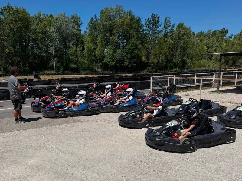 Groupe de personnes en karts alignés sur une piste, un instructeur debout à côté, sous un ciel clair.