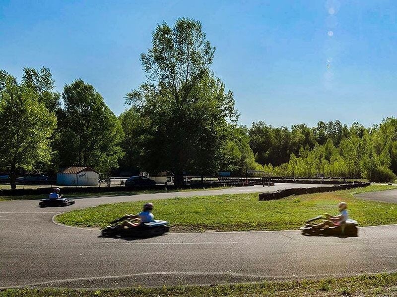 Deux karts en mouvement sur une piste de karting avec des arbres et un ciel bleu en arrière-plan.