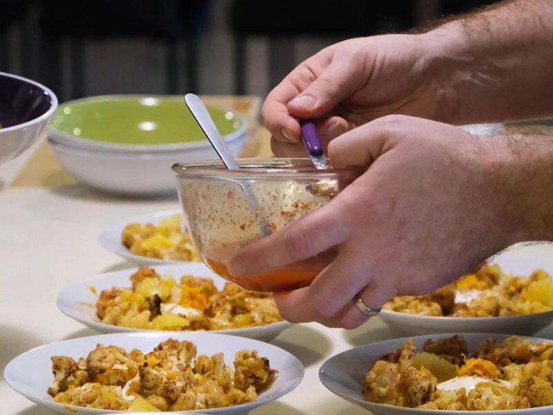 Un cuisinier prépare plusieurs assiettes avec un plat à base de légumes et viande sur une table blanche.