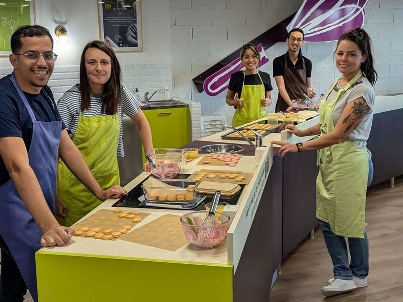 Quatre participants souriants portant des tabliers posent dans une cuisine moderne avec des ingrédients devant eux.