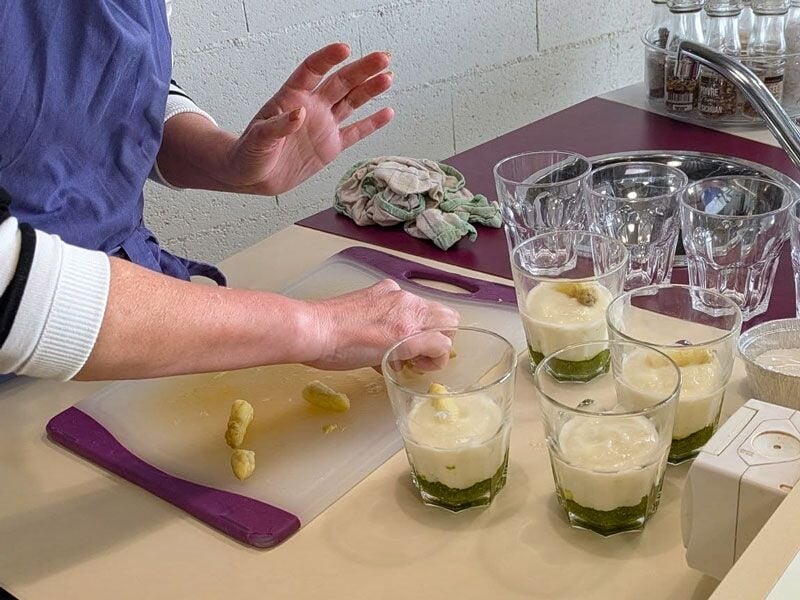 Une personne prépare des verrines avec une mousse blanche et une base verte sur un plan de travail.