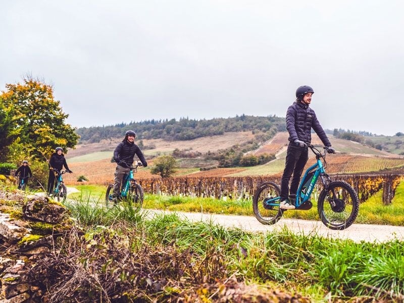 Groupe de cyclistes sur des vélos électriques sur une route de campagne entourée de collines et de vignes en automne.