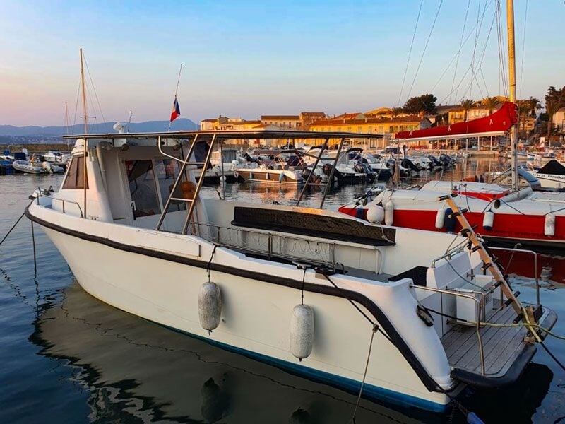 Bateau blanc amarré dans un port au coucher du soleil, avec plusieurs autres bateaux visibles en arrière-plan.