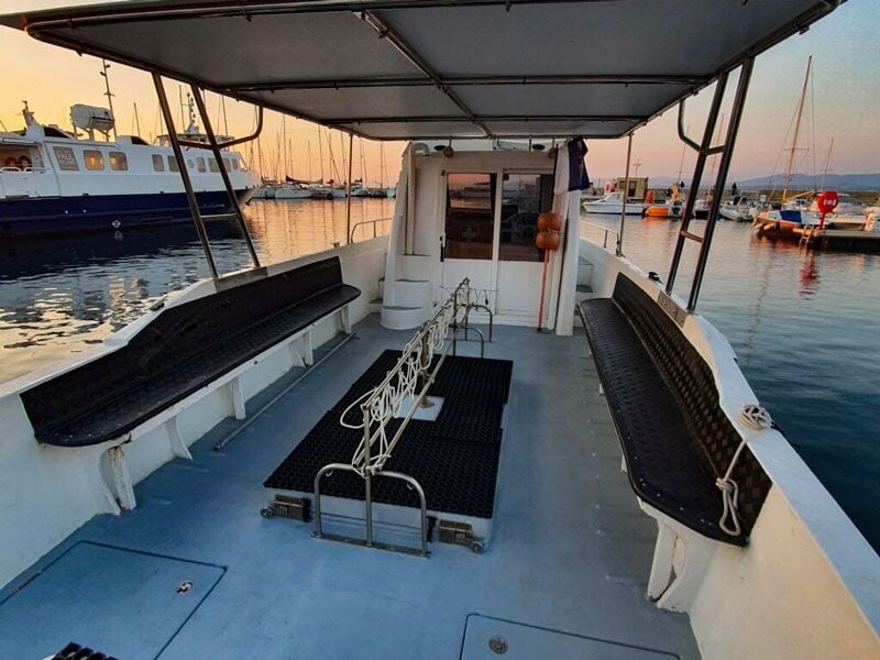 Pont d'un bateau de plongée avec bancs latéraux et espace central dégagé, au port au crépuscule.