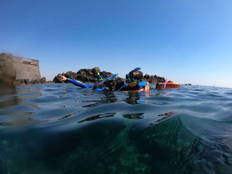 Groupe de plongeurs en combinaison et masque de plongée nageant à la surface de l'eau près d'un fort.