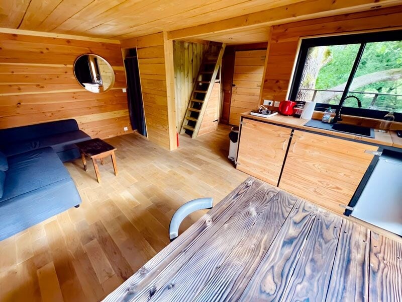 Intérieur d'une cabane en bois avec canapé bleu, table en bois et kitchenette moderne.