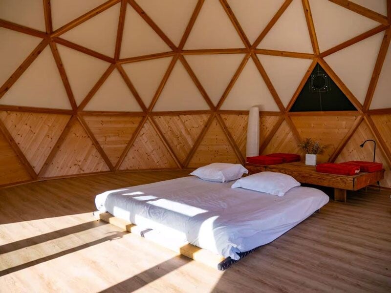 Chambre spacieuse avec lit au sol, murs en bois et plafond géodésique lumineux.