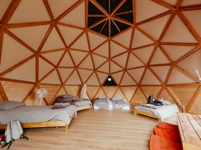 Grande pièce ronde avec plusieurs lits simples, murs en bois et plafond géodésique.