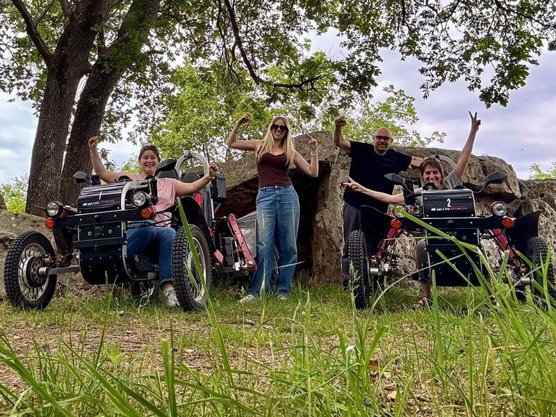 Quatre personnes souriantes posent avec deux véhicules électriques tout-terrain Swincar dans un cadre naturel verdoyant.