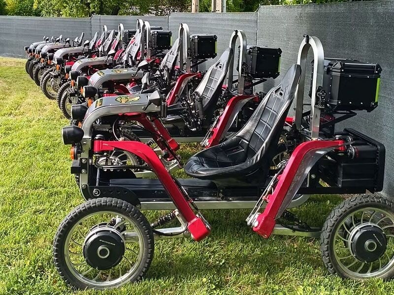 Alignement de plusieurs véhicules électriques tout-terrain Swincar rouges et noirs garés sur une pelouse devant une clôture.