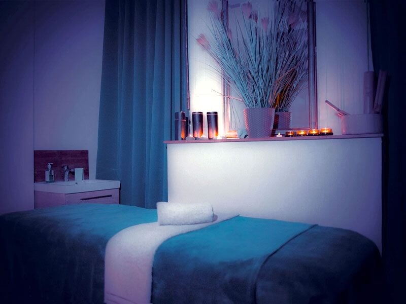 Salle de massage tamisée avec table recouverte d'une couverture bleue, bougies allumées et décor apaisant.