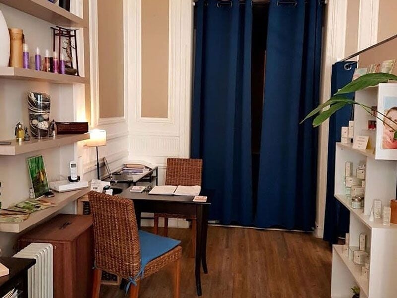 Coin bureau chaleureux avec chaise en osier, table noire, étagères blanches et rideaux bleus dans une pièce accueillante.