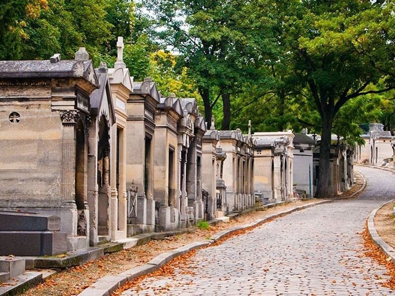 Allée pavée bordée de tombes anciennes et de mausolées dans le cimetière du Père Lachaise à Paris, sous un ciel clair.