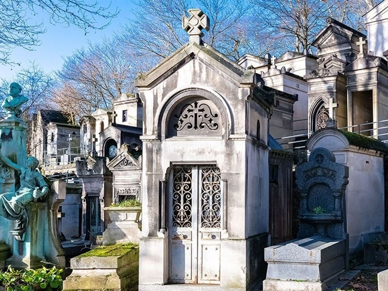 Mausolée en pierre avec porte en fer forgé et sculptures dans le cimetière du Père Lachaise, entouré d'autres tombes.