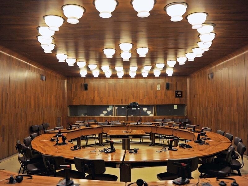Salle de réunion circulaire en bois avec des chaises et un éclairage en forme d'anneau au plafond.